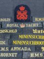 Wandbehang aus etwa 202 Mützenbändern sowie diversen Ärmelabzeichen. Dekorativ