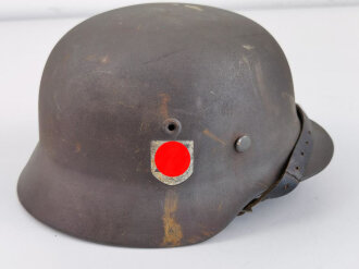 Stahlhelm Modell 1940 der Wehrmacht. Vermutlich in Teilen originales Innenfutter, Nieten und Glocke SE64. Neuzeitlich lackiert und mit Emblemen der Waffen SS versehen, der Kinnriemen ist ebenfalls eine Reproduktion.