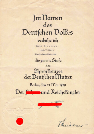 Ehrenkreuz der Deutschen Mutter zweite Stufe, in Tüte von Gottlieb & Wagner Oberstein. Dazu die zugehörige Verleihungsurkunde sowie Einladung zur Feierstunde der NSDAP Ortsgruppe Wiesbaden Biebrich mit eigenhändiger Unterschrift des Ortsgruppenleiter