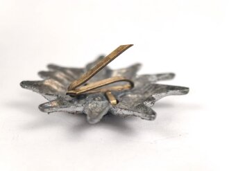 Traditionsedelweiss für die Schirmmütze von Angehörigen der Gebirgstruppe der Wehrmacht. Wird zwischen Eichenlaub und Adler getragen. Fertigung aus Zink, versilbert